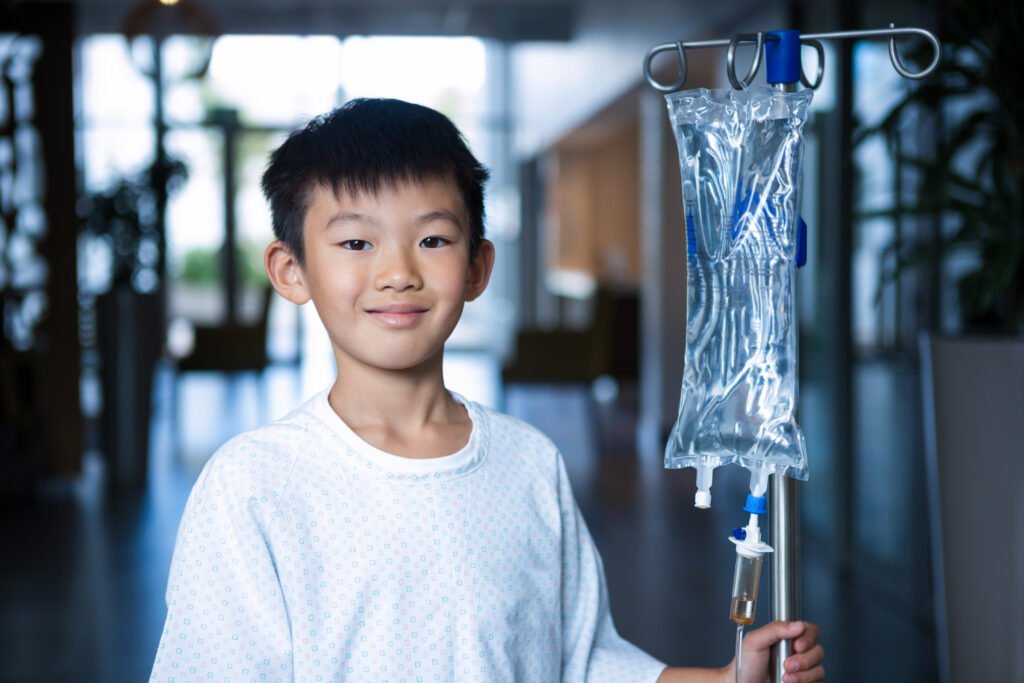 Smiling boy patient holding intravenous iv drip stand in corridor - Hope Foundation of the Mahoning Valley