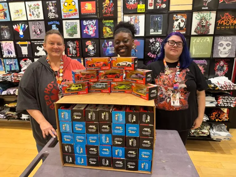 Two people posing with donated toy car boxes from FYE